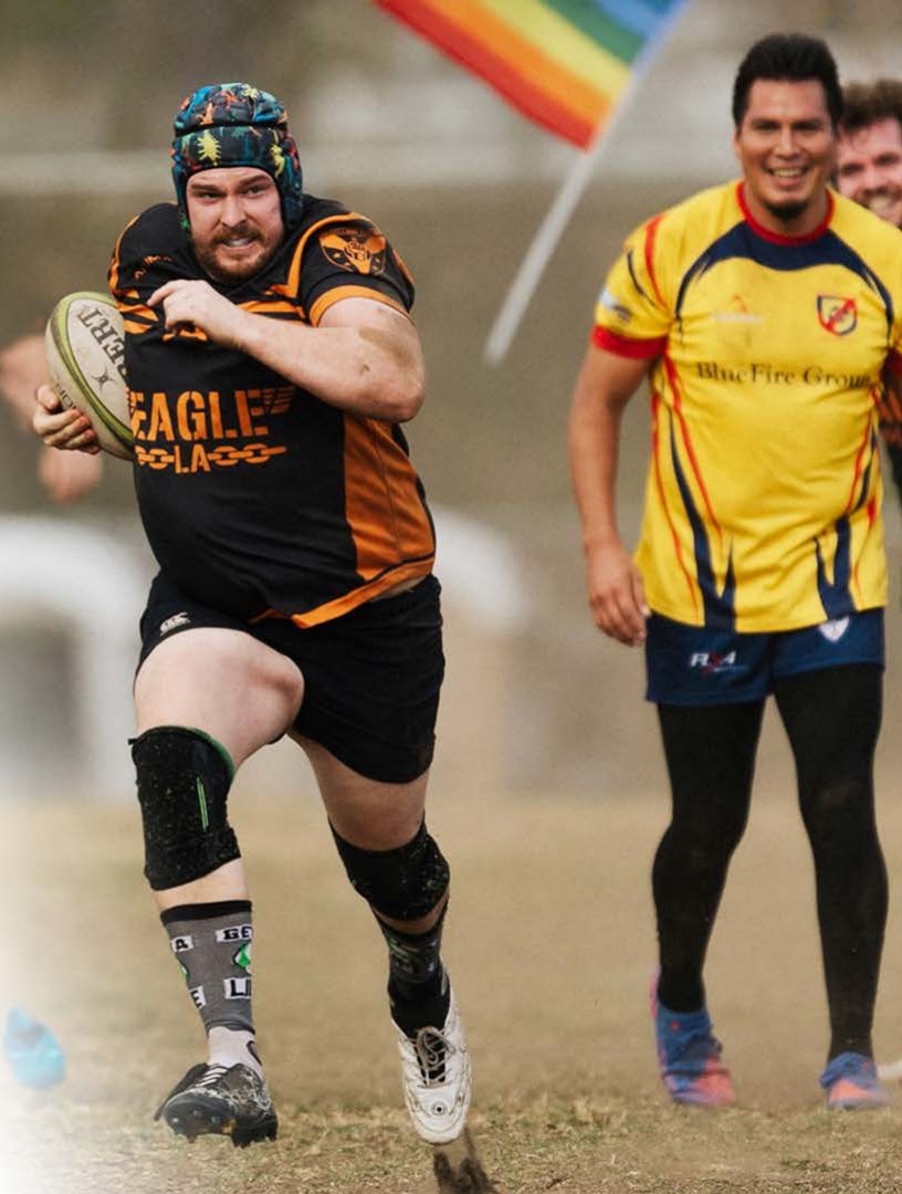 Gay rugby players running with the ball under a Pride flag